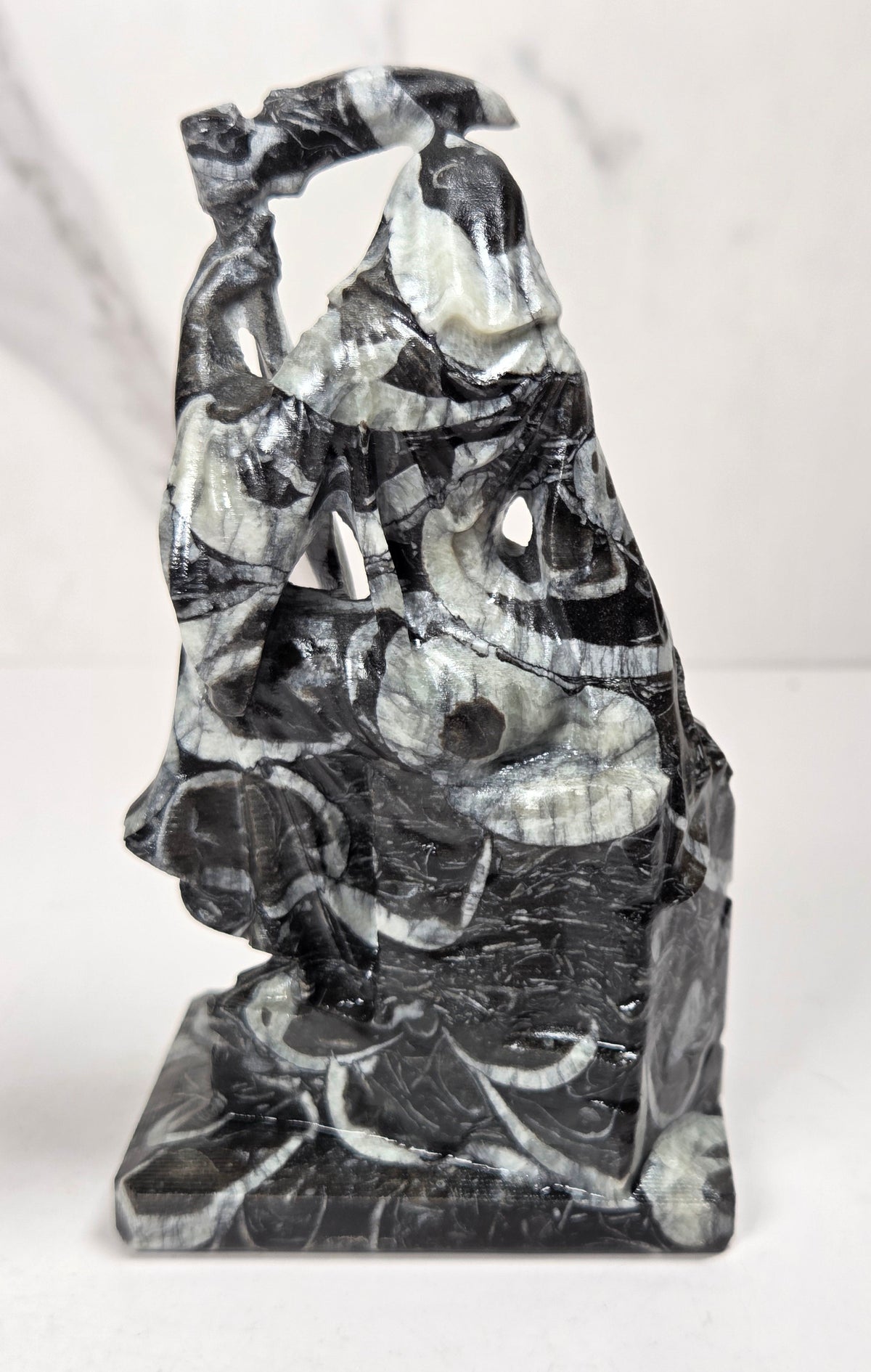 faceless lady reaper carving made of a marbled black and white mineral against a marbled white background