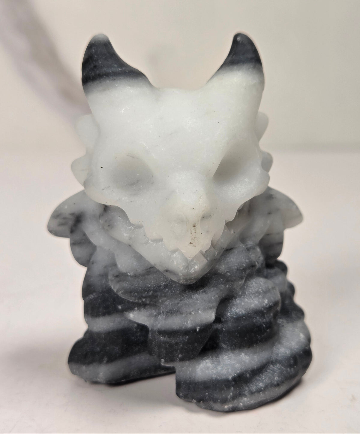 Stylized carving of a character with a skull made of black, white and grey crystal against a white background