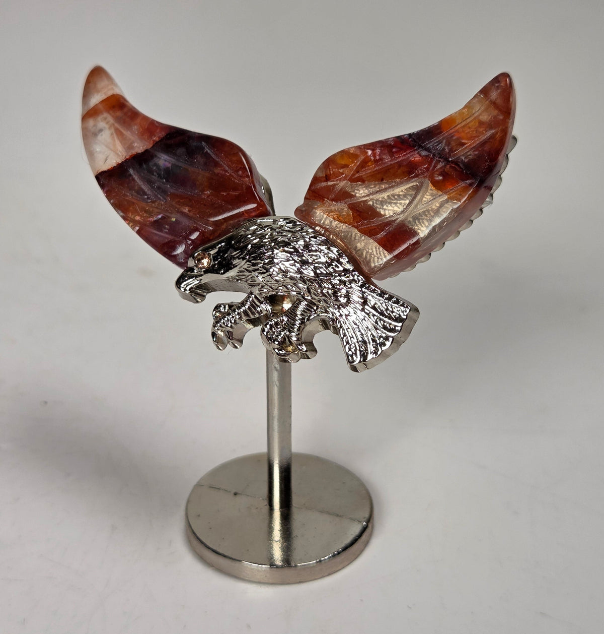 Red fire quartz crystal wings with a silver eagle on a silver stand against a white background