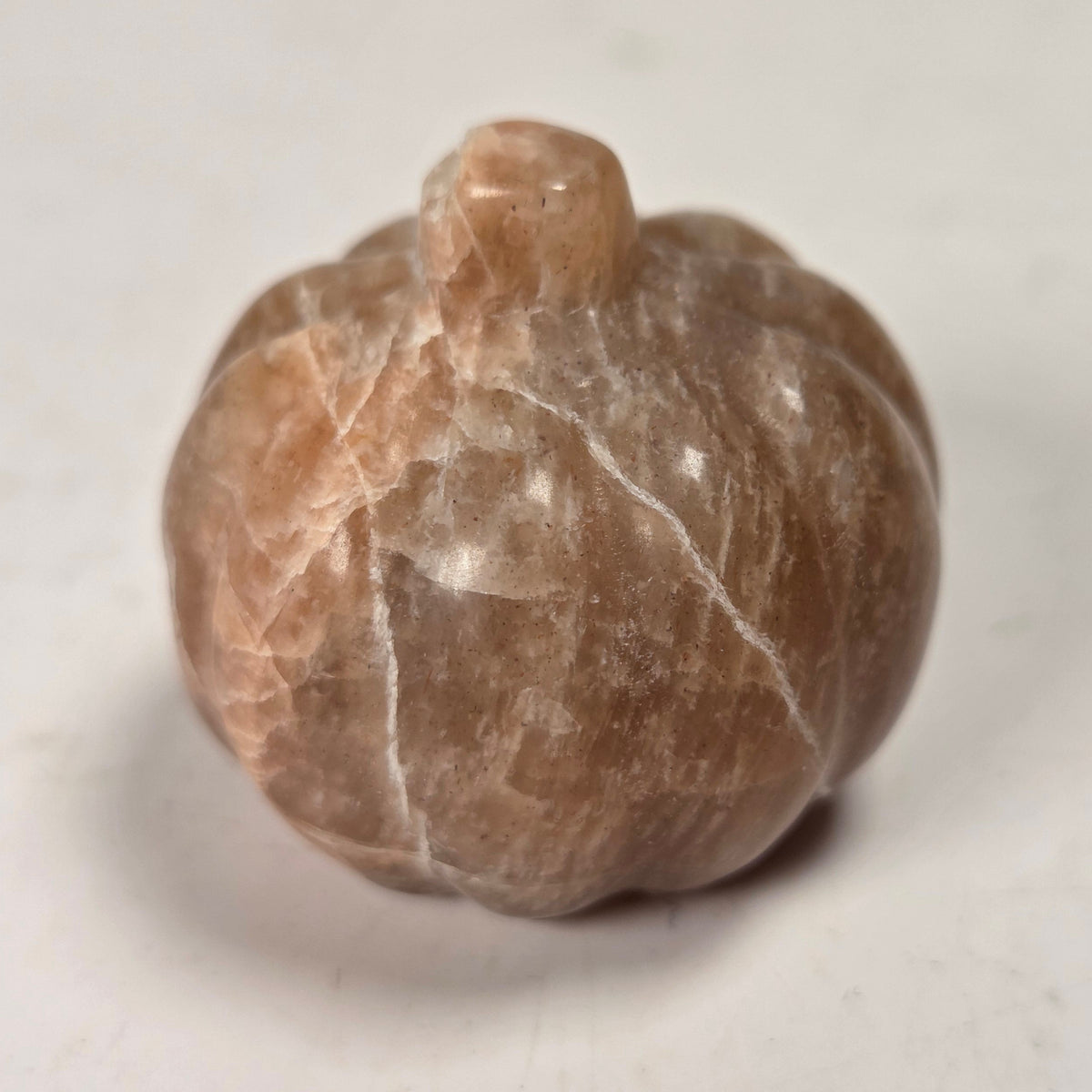 Polished peach crystal pumpkin carving against a white background
