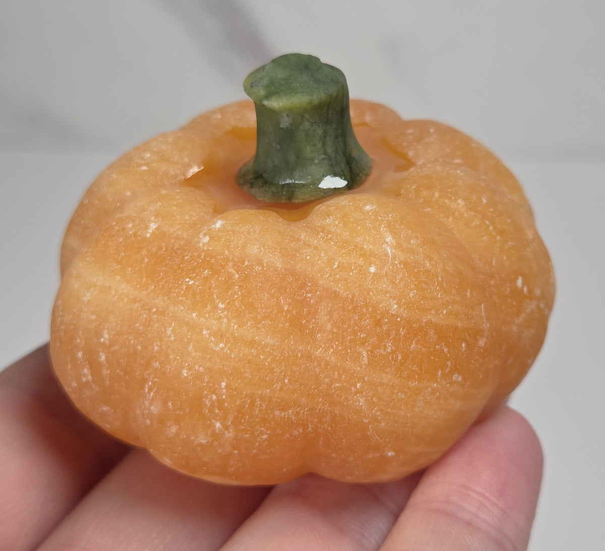 Hand holding an Orange calcite pumpkin carvings with green jade stems against a white background