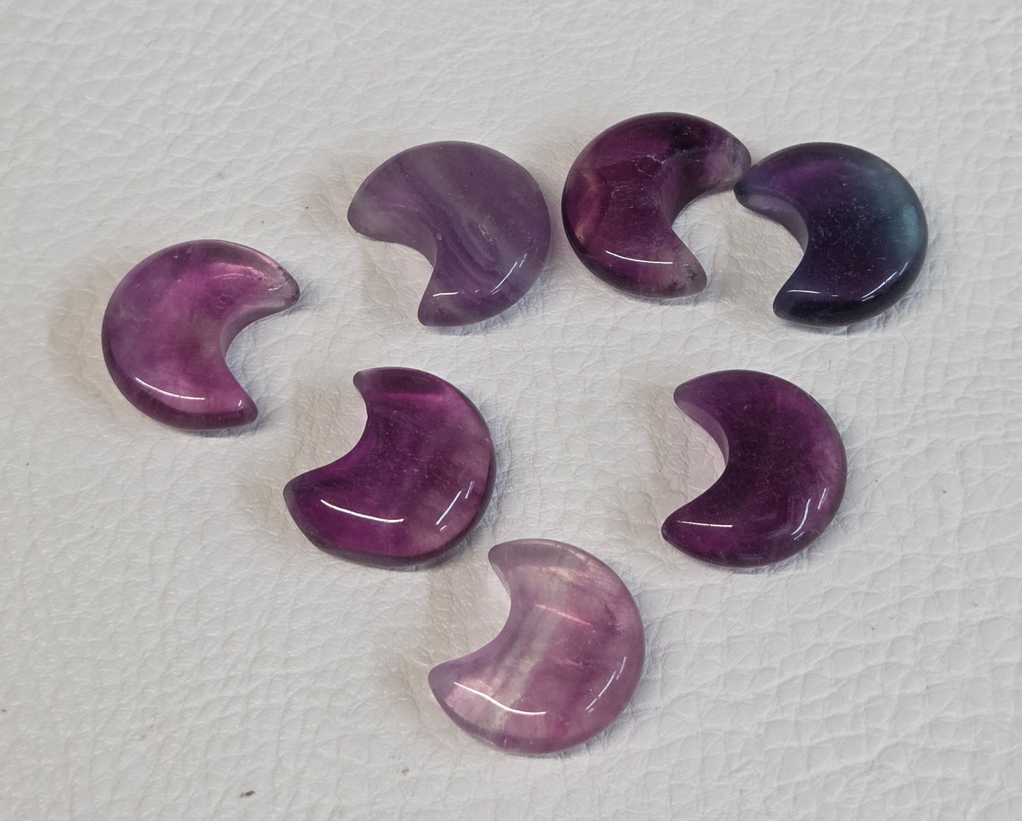 Set of purple Fluorite mini moon-shaped stones on a textured white surface