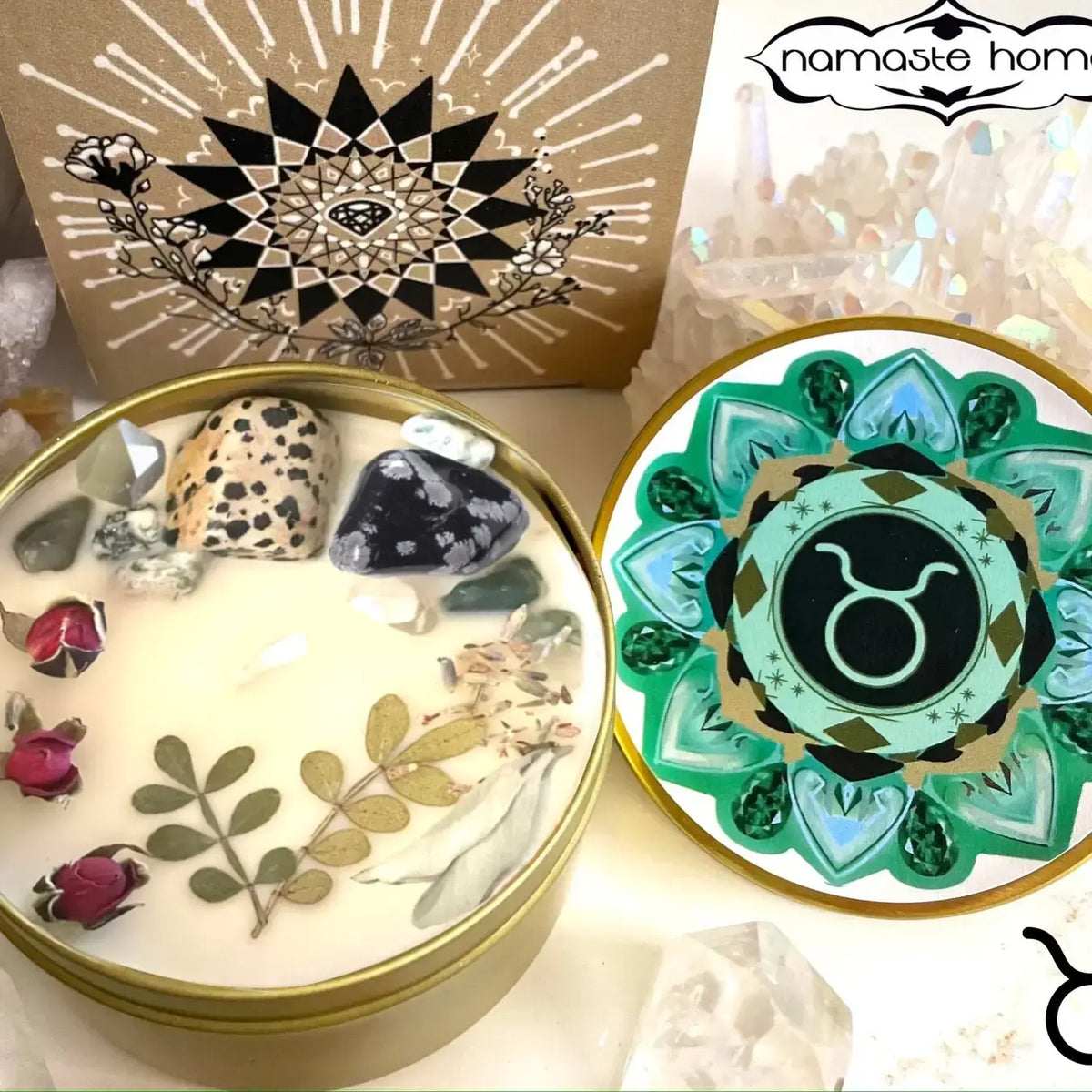 A decorative circular candle tin shown open, with a matching round lid placed beside it. The candle wax contains pressed botanical elements and stones, and the lid features a teal, green, black, and gold mandala-style design with the Libra zodiac symbol in the center.