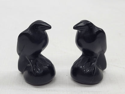 Two small obsidian raven carvings placed back to back on a plain surface.