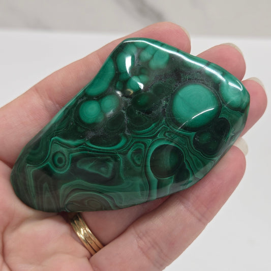 Hand holding a green malachite stone against a white background