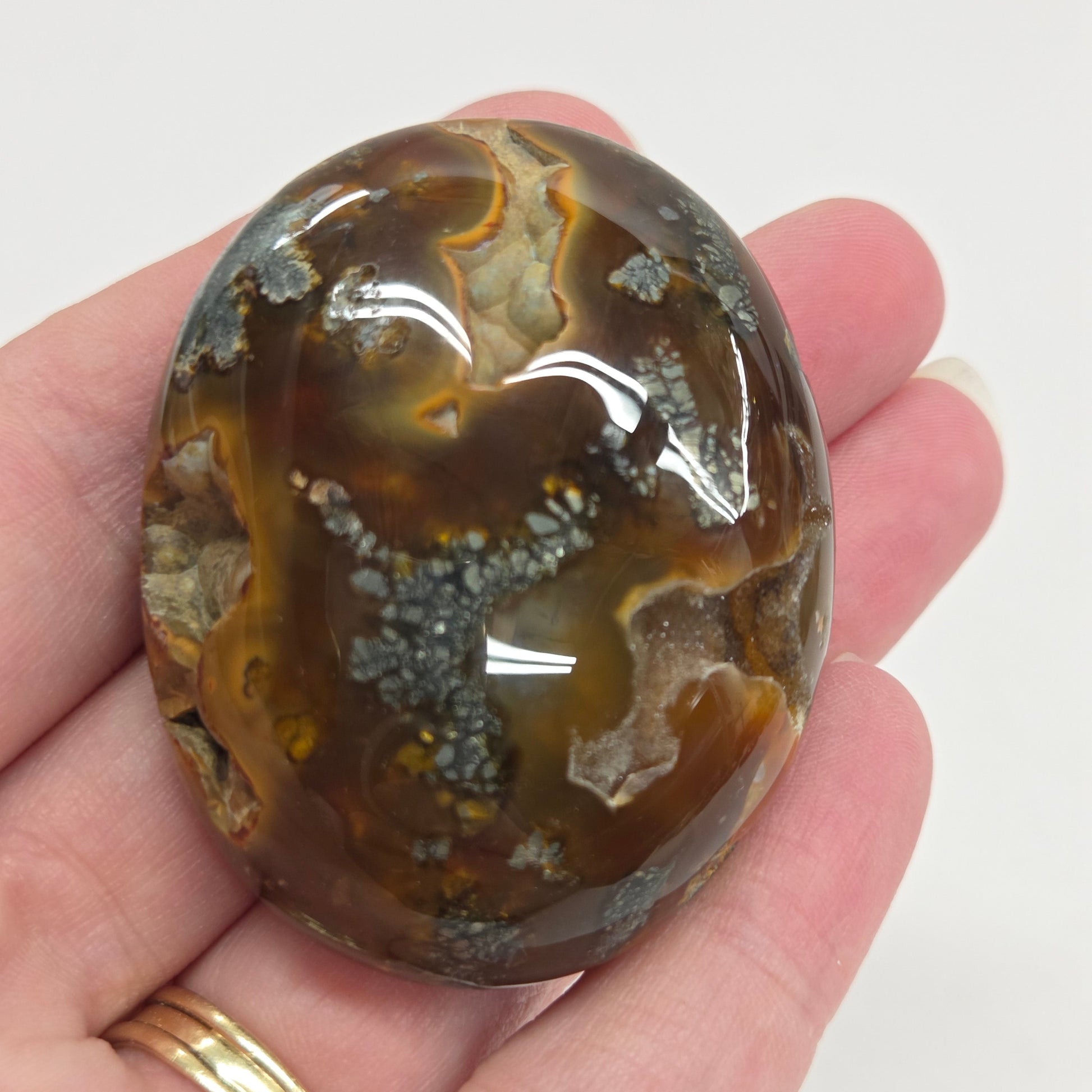 Hand holding a polished marcasite stone with various shades of red, orange, gold, and gray, displayed on a white surface.
