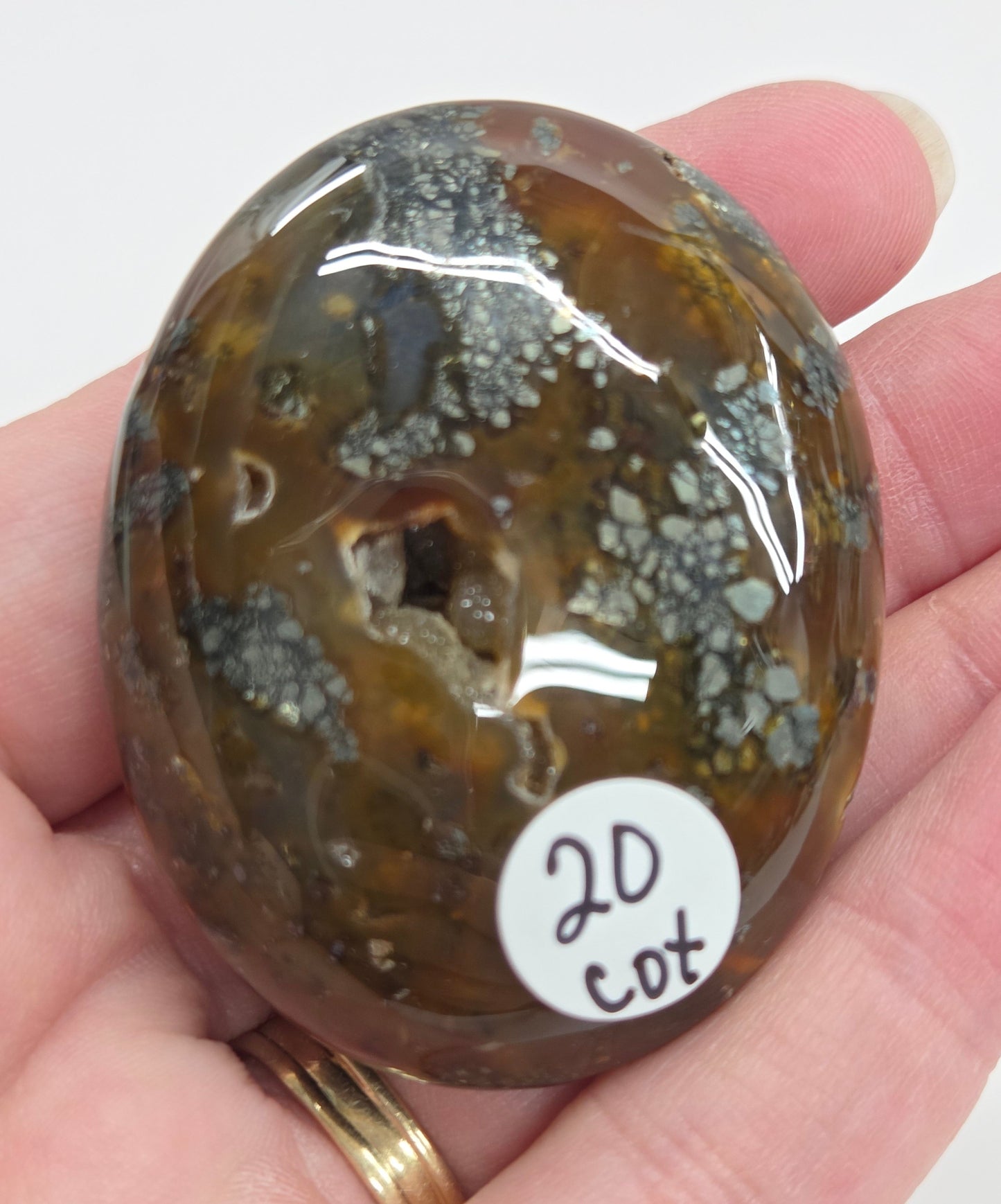 Hand holding a polished marcasite stone with various shades of red, orange, gold, and gray, displayed on a white surface.