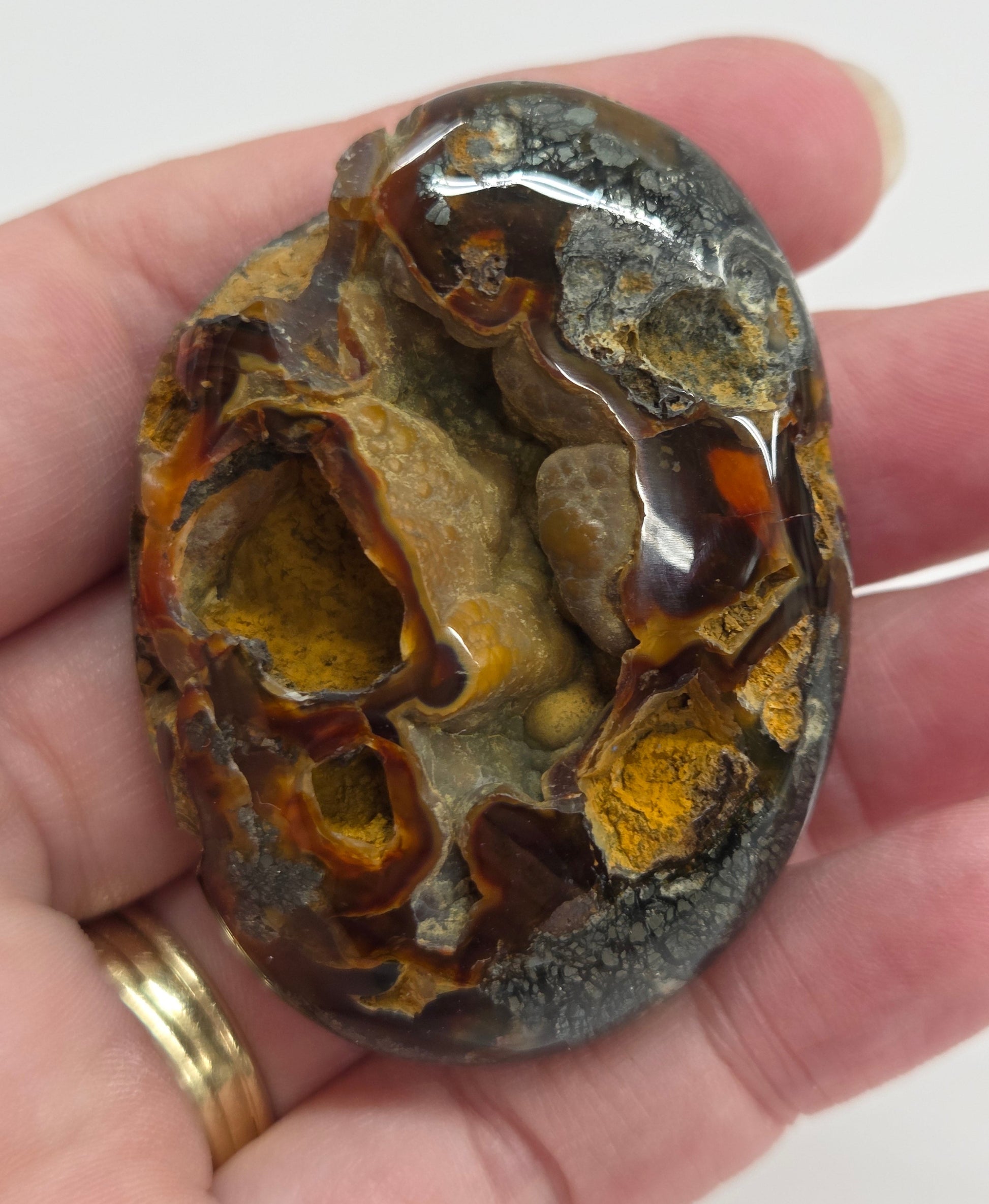 Hand holding a polished marcasite stone with various shades of red, orange, gold, and gray, displayed on a white surface.