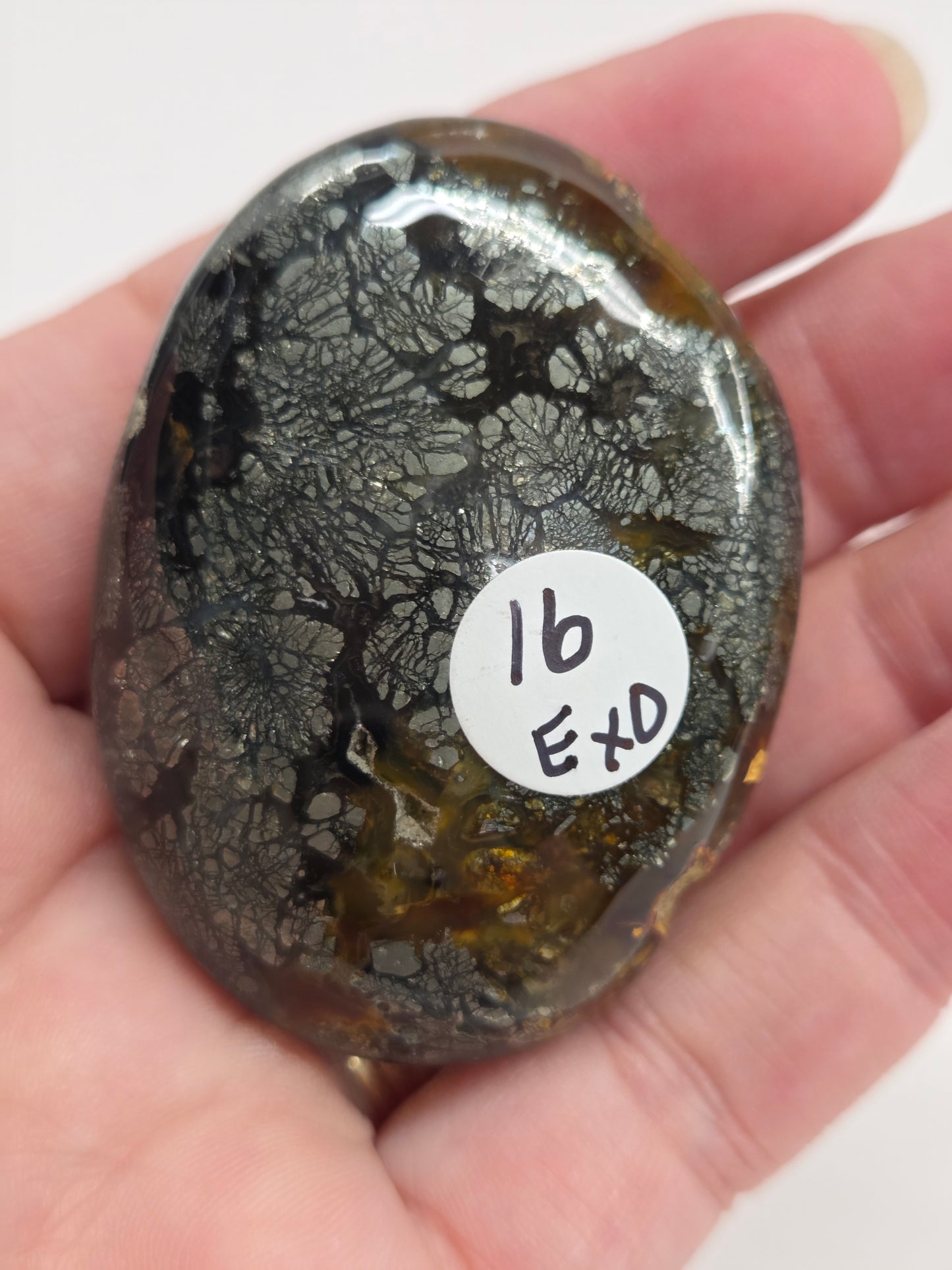 Hand holding a polished marcasite stone with various shades of red, orange, gold, and gray, displayed on a white surface.