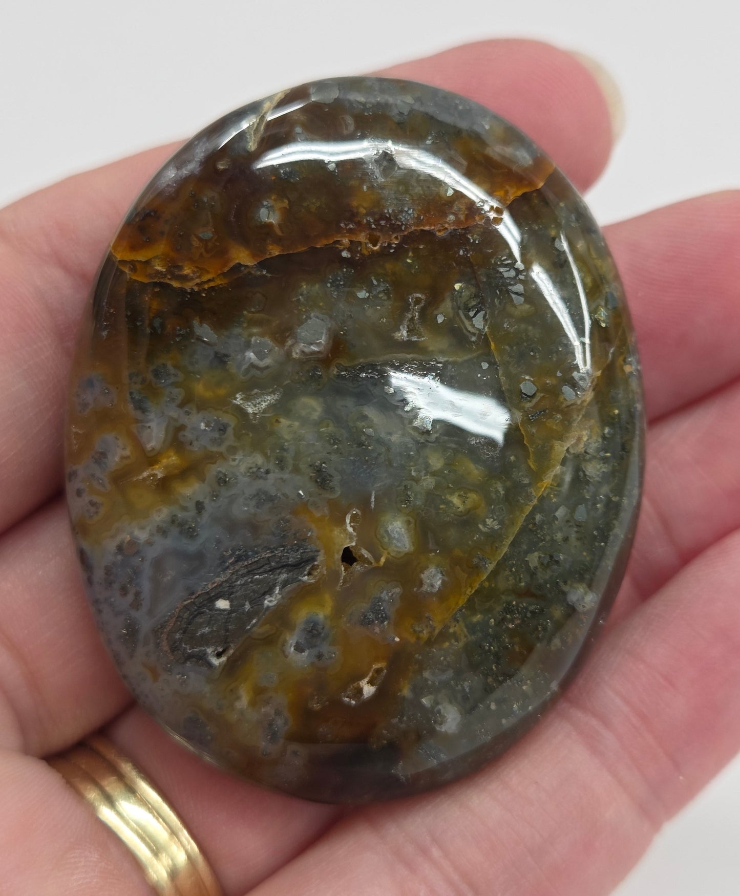 Hand holding a polished marcasite stone with various shades of red, orange, gold, and gray, displayed on a white surface.