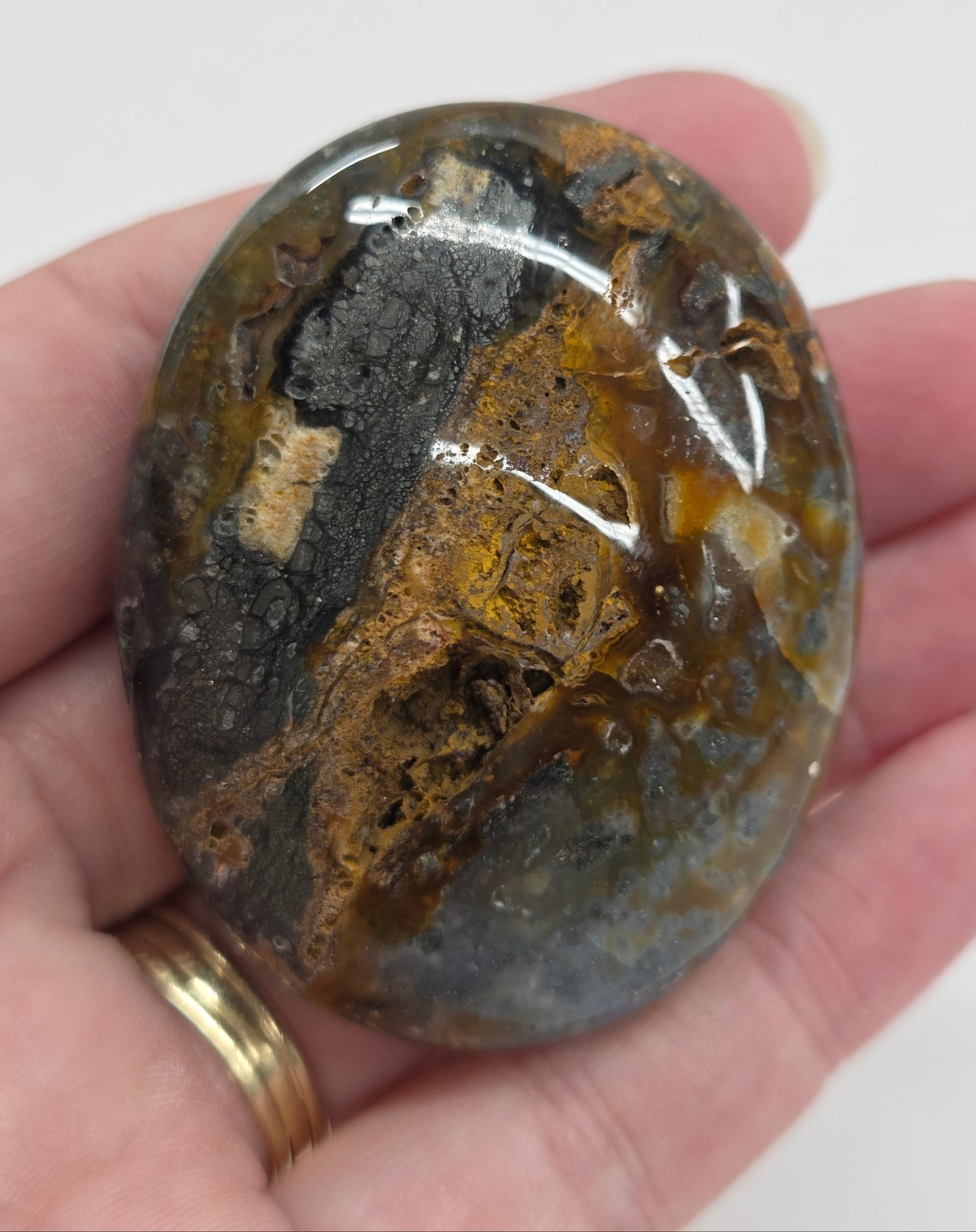 Hand holding a polished marcasite stone with various shades of red, orange, gold, and gray, displayed on a white surface.