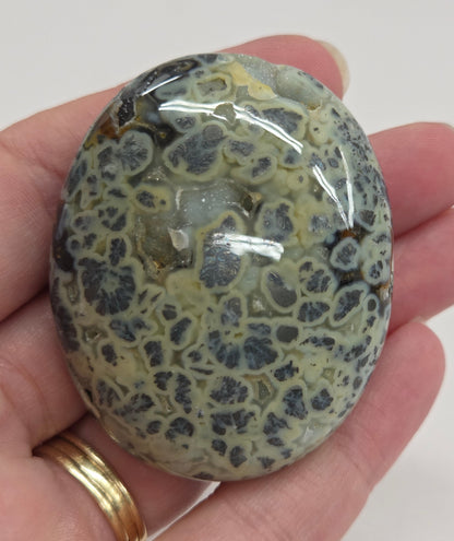 Hand holding a polished marcasite stone with various shades of red, orange, gold, and gray, displayed on a white surface.