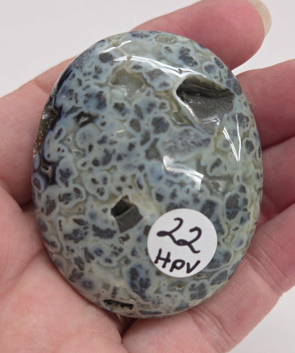Hand holding a polished marcasite stone with various shades of red, orange, gold, and gray, displayed on a white surface.