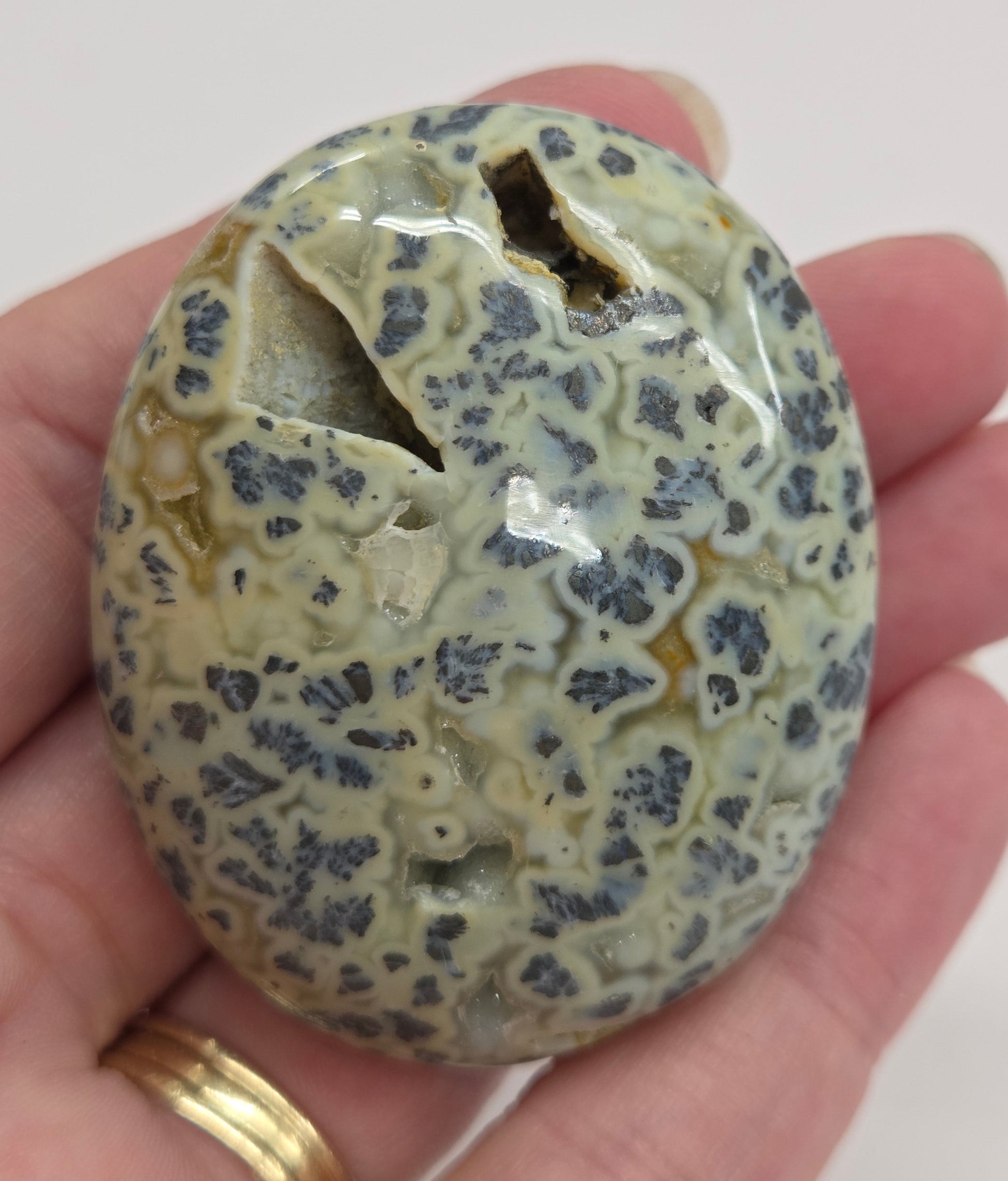 Hand holding a polished marcasite stone with various shades of red, orange, gold, and gray, displayed on a white surface.