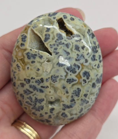 Hand holding a polished marcasite stone with various shades of red, orange, gold, and gray, displayed on a white surface.