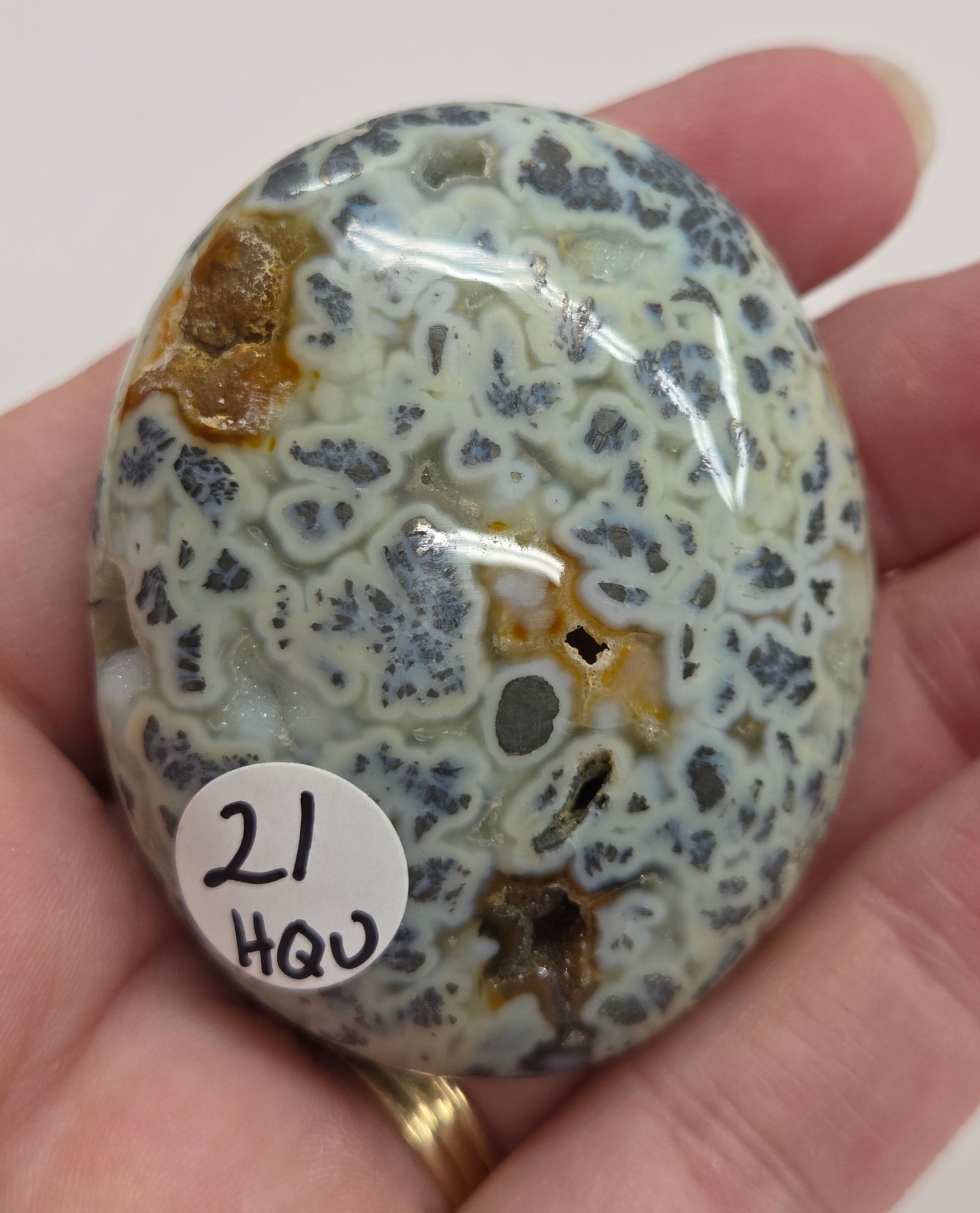 Hand holding a polished marcasite stone with various shades of red, orange, gold, and gray, displayed on a white surface.
