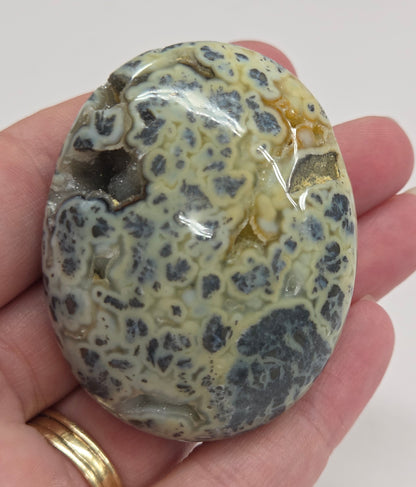 Hand holding a polished marcasite stone with various shades of red, orange, gold, and gray, displayed on a white surface.