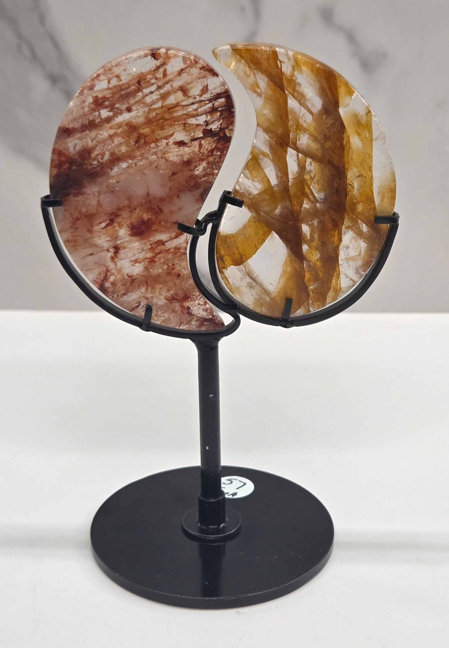 Two stones carved into a yin yang symbol, one fire quartz, one golden healer, on a black stand against a marble background