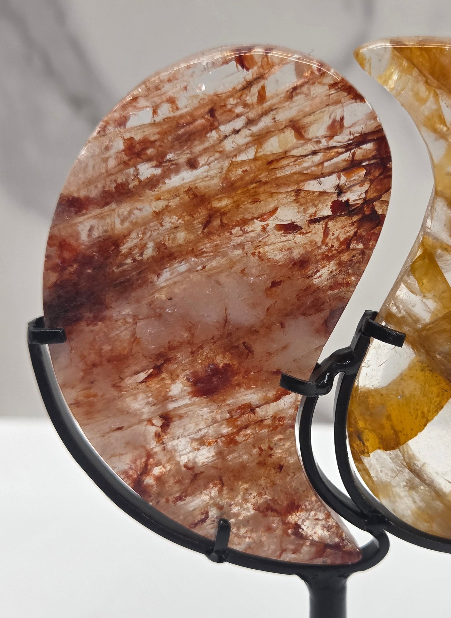 Two stones carved into a yin yang symbol, one fire quartz, one golden healer, on a black stand against a marble background