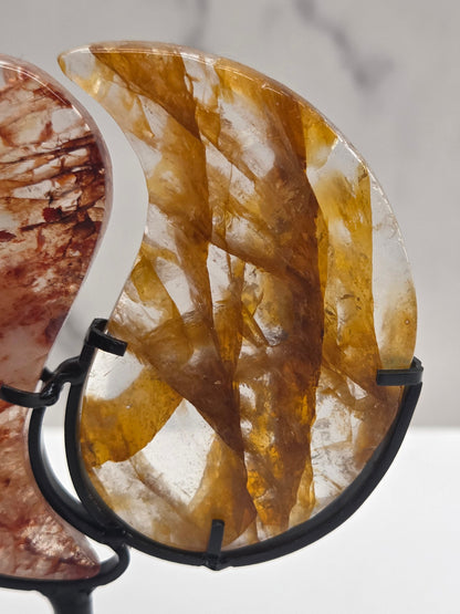Two stones carved into a yin yang symbol, one fire quartz, one golden healer, on a black stand against a marble background