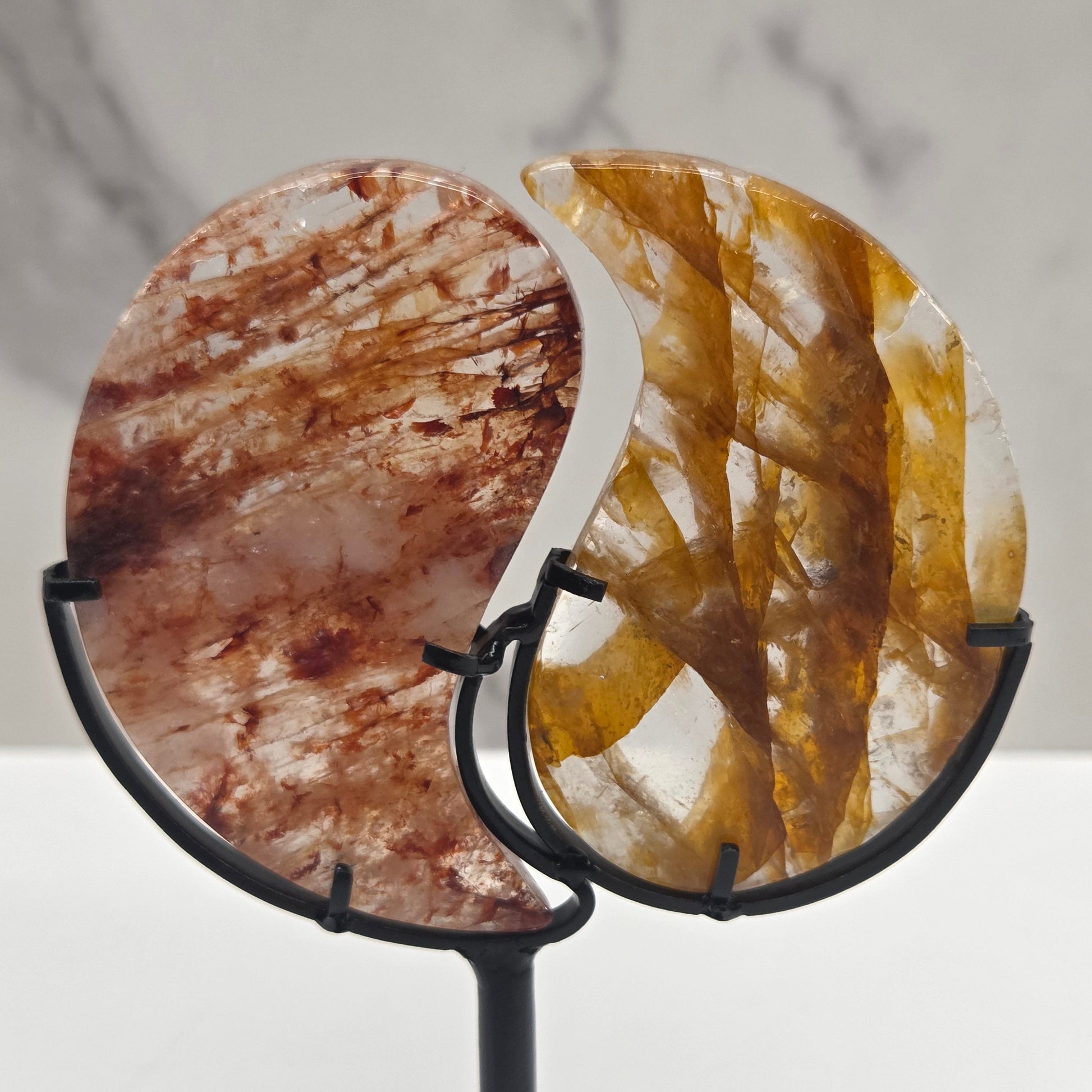 Two stones carved into a yin yang symbol, one fire quartz, one golden healer, on a black stand against a marble background