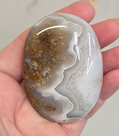 Hand holding a Scenic Moss Agate palm with white, yellow, red and brown coloring on a white background