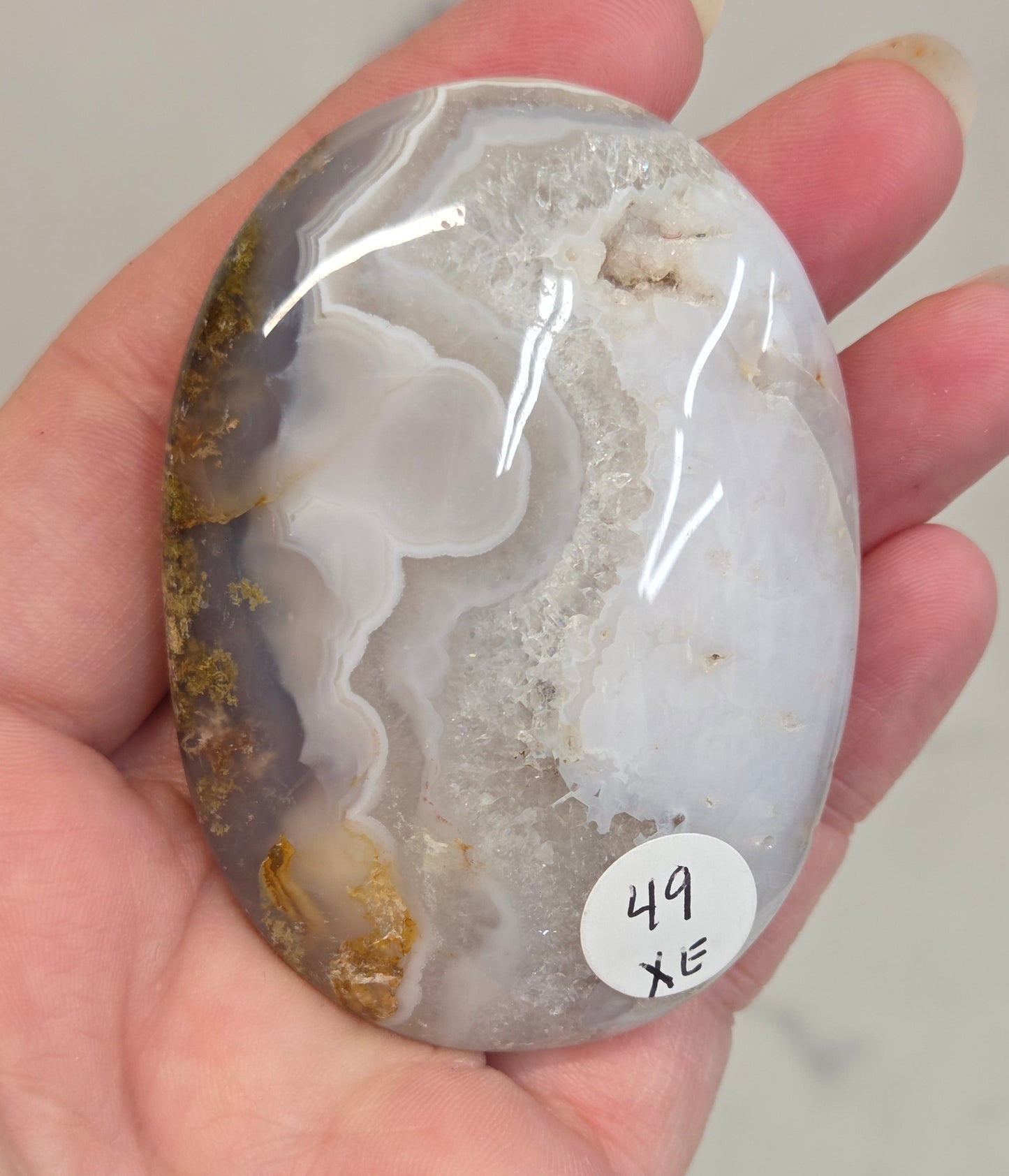 Hand holding a Scenic Moss Agate palm with white, yellow, red and brown coloring on a white background