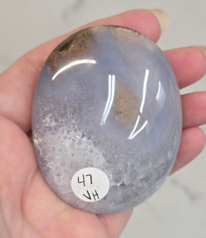 Hand holding a Scenic Moss Agate palm with white, yellow, red and brown coloring on a white background