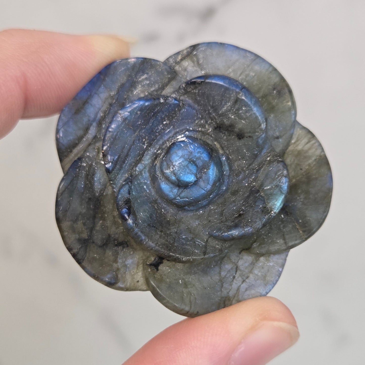 Hand holding a Labradorite rose-shaped carving on a light gray background
