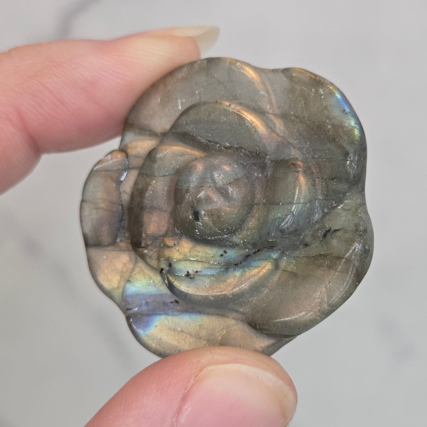 Hand holding a Labradorite rose-shaped carving on a light gray background