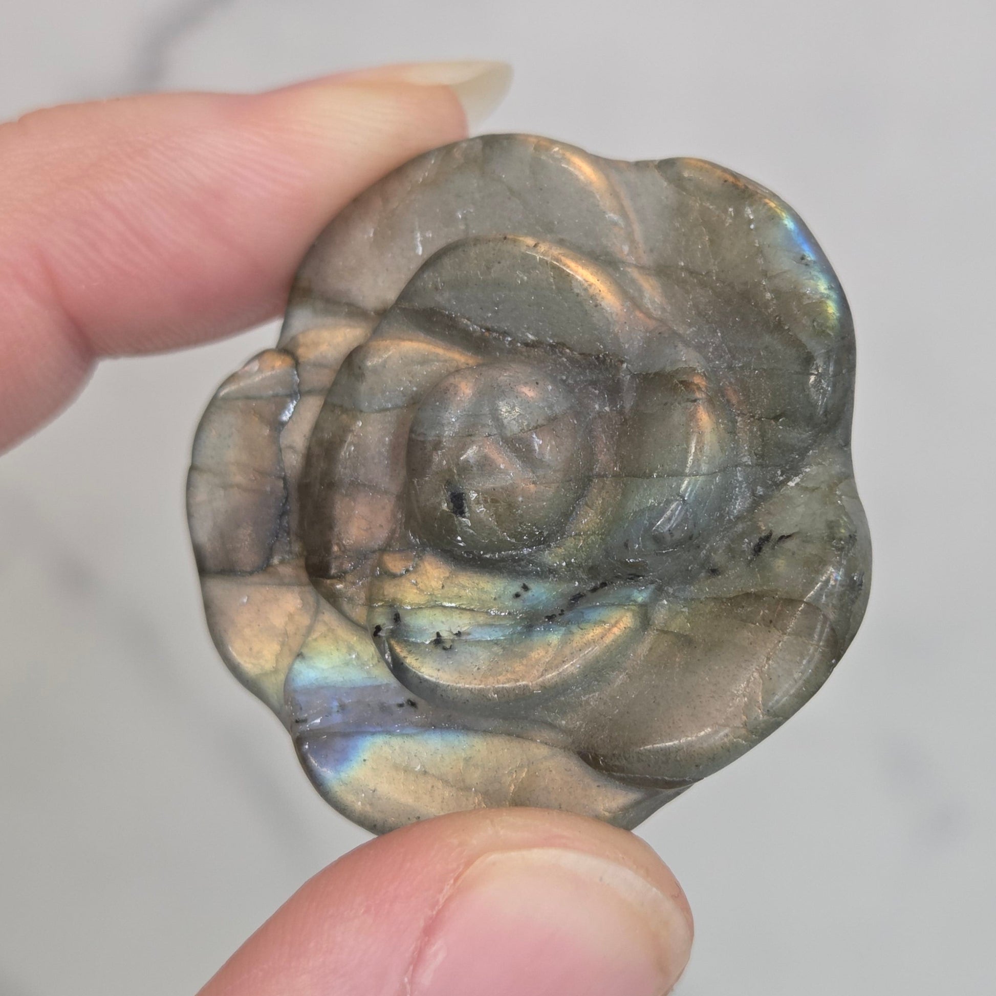Hand holding a Labradorite rose-shaped carving on a light gray background
