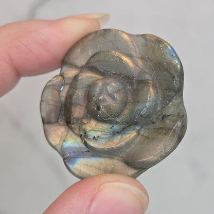 Hand holding a Labradorite rose-shaped carving on a light gray background
