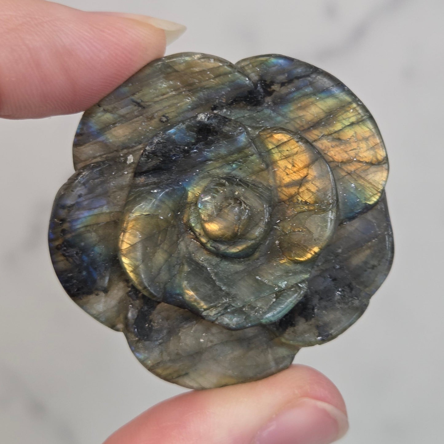 Hand holding a Labradorite rose-shaped carving on a light gray background