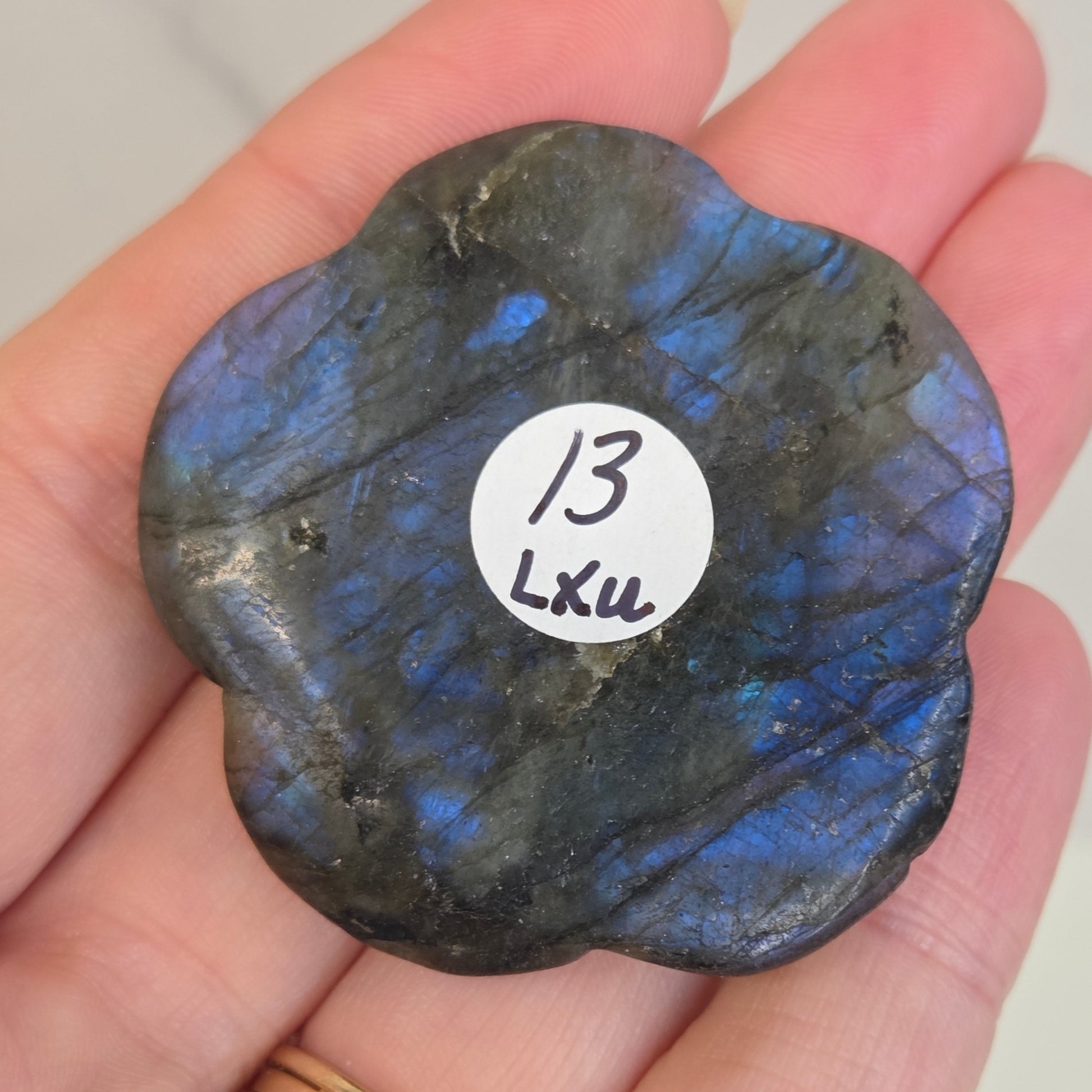 Hand holding a Labradorite rose-shaped carving on a light gray background