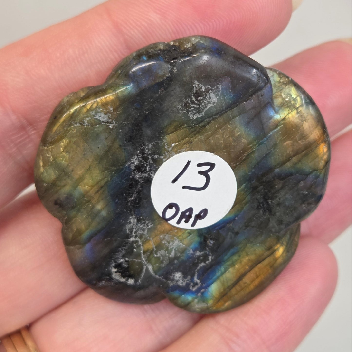 Hand holding a Labradorite rose-shaped carving on a light gray background