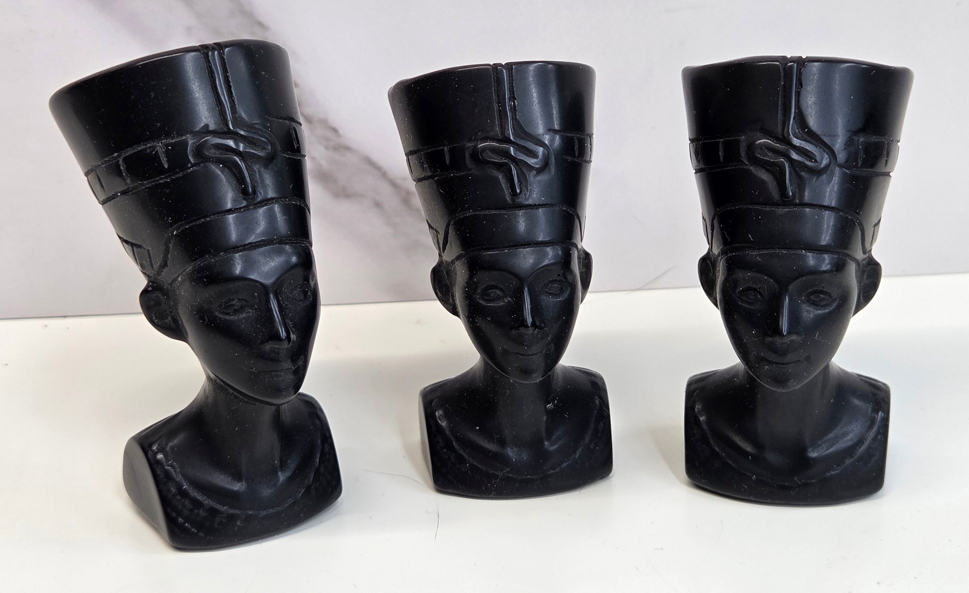 Three black Obsidian Nefertiti busts with decorative patterns on a white surface.