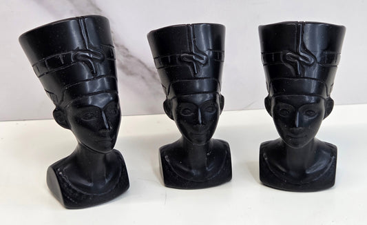 Three black Obsidian Nefertiti busts with decorative patterns on a white surface.
