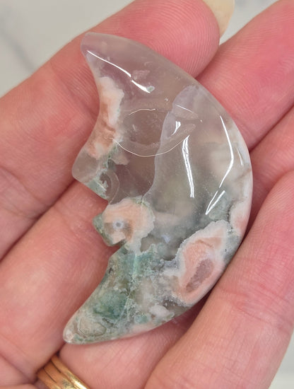 Flower Agate moon carving with a carved face held in a hand against a white background