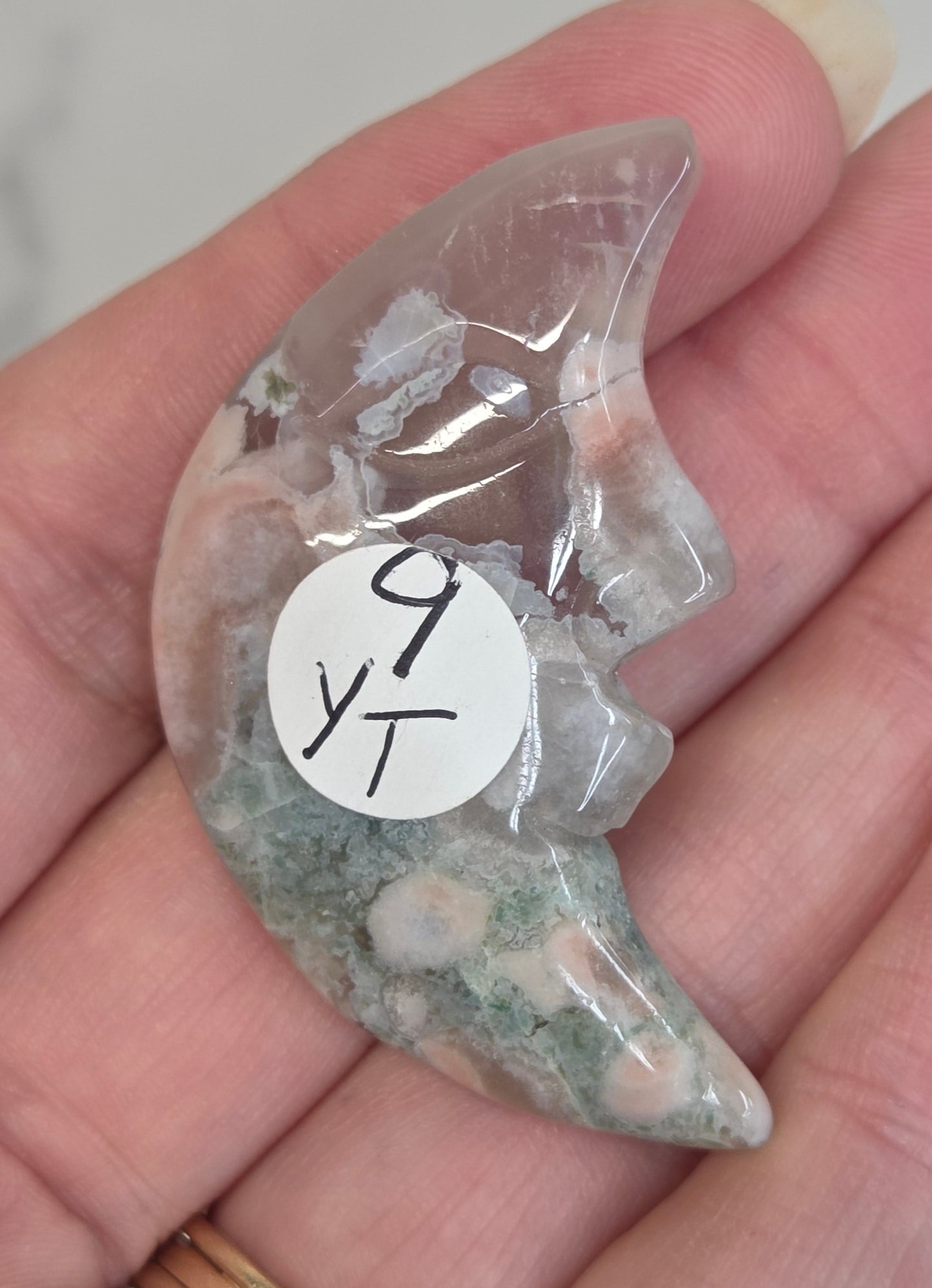 Flower Agate moon carving with a carved face held in a hand against a white background