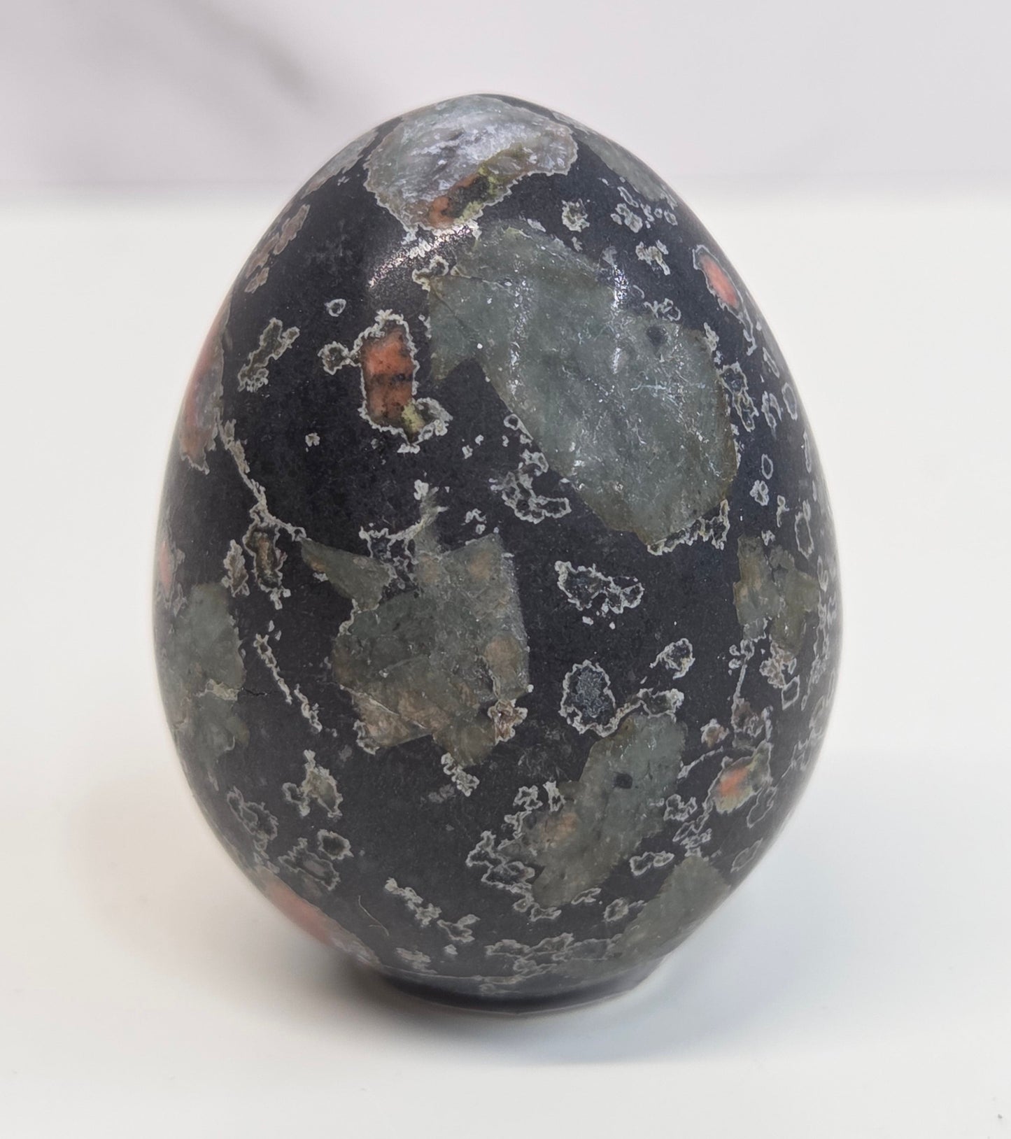 Plum Blossom Jasper polished egg carving with red and green patterns on a white background