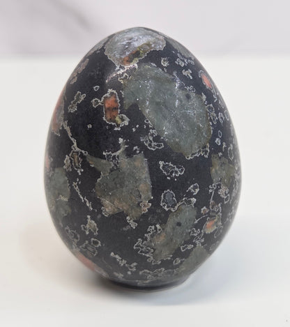 Plum Blossom Jasper polished egg carving with red and green patterns on a white background