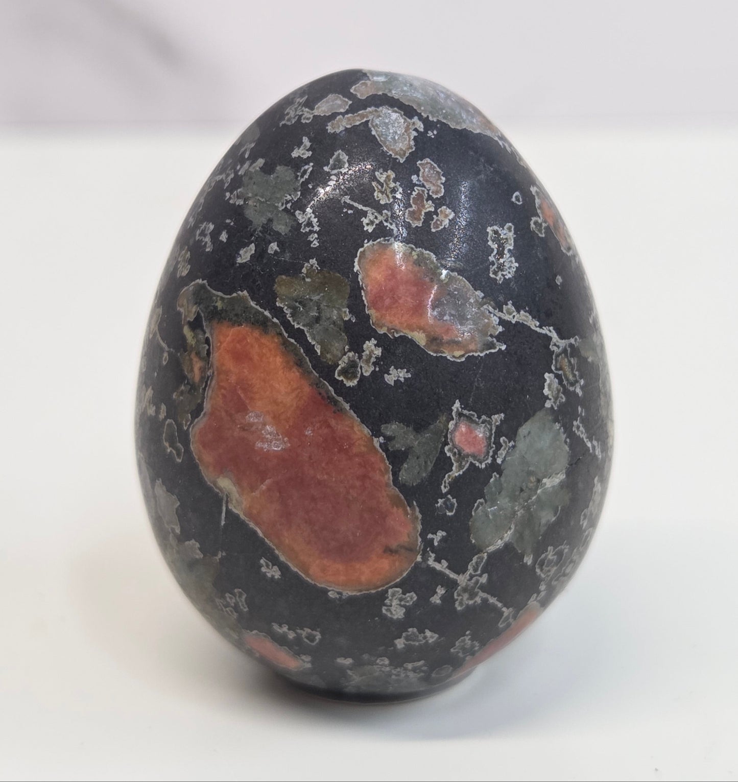 Plum Blossom Jasper polished egg carving with red and green patterns on a white background