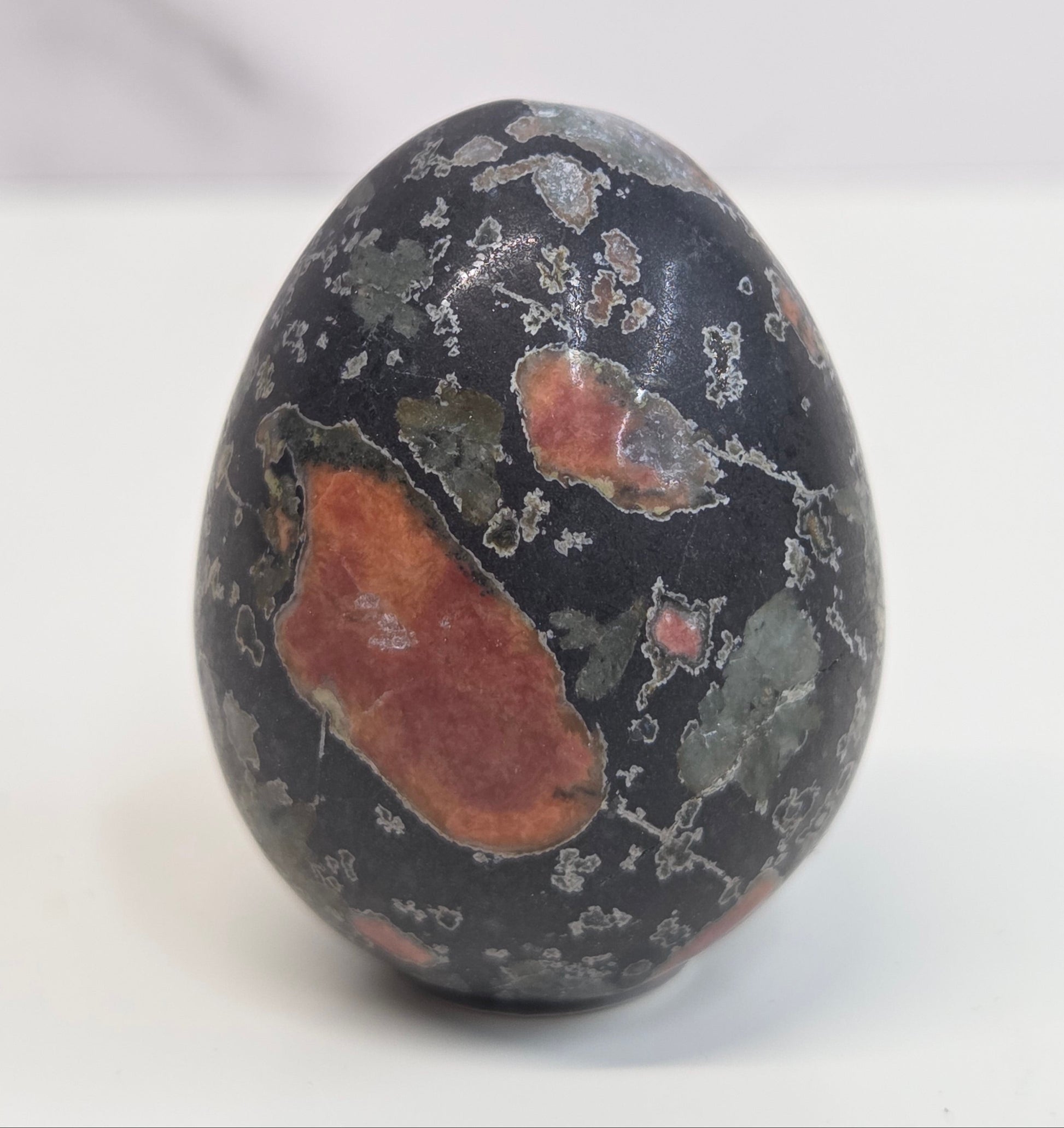 Plum Blossom Jasper polished egg carving with red and green patterns on a white background