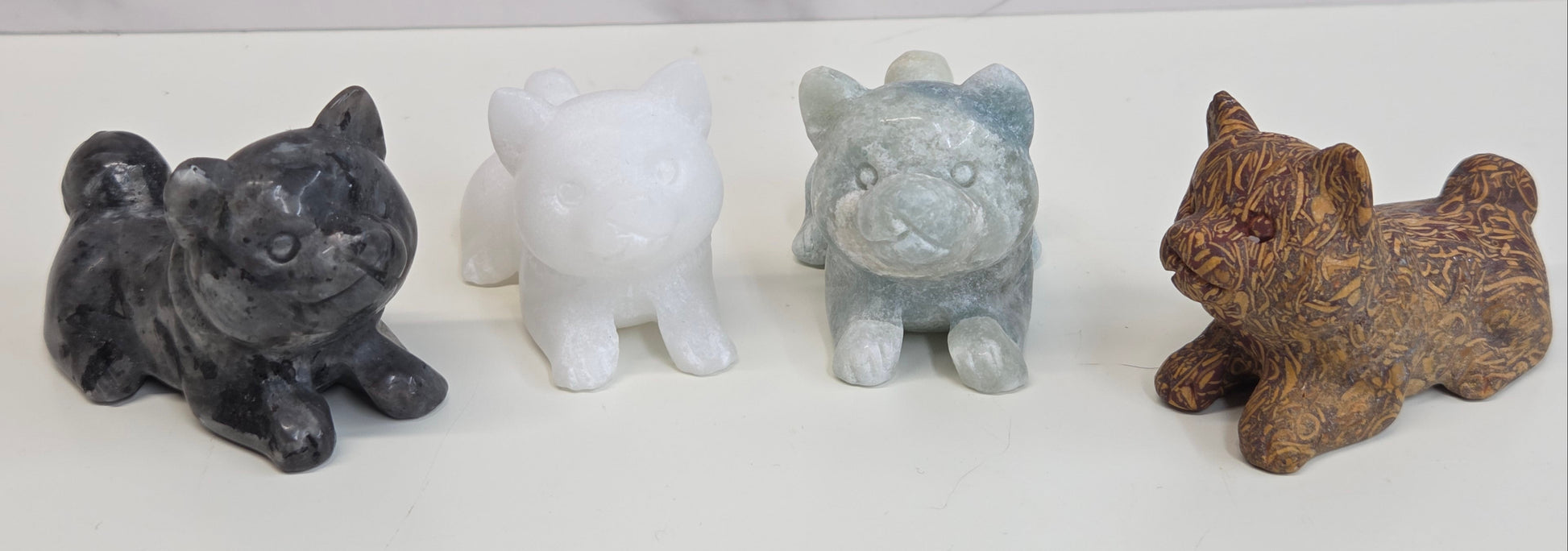 Four small stone dog figurines of different colors on a white background