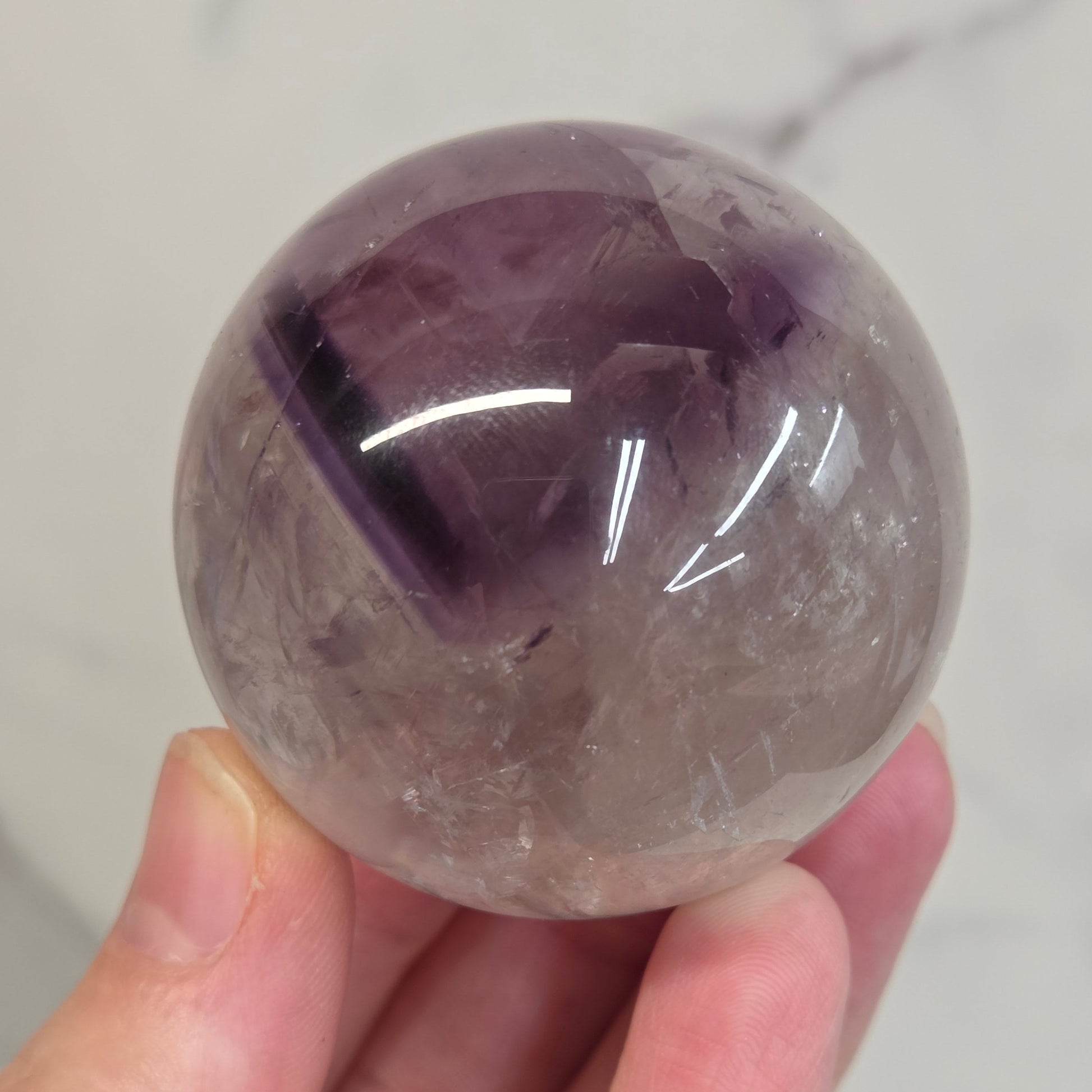 Hand holding a Phantom Amethyst sphere on a white background