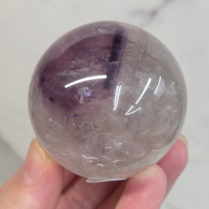 Hand holding a Phantom Amethyst sphere on a white background