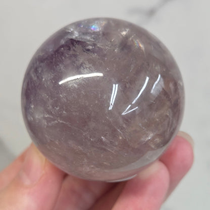 Hand holding a Phantom Amethyst sphere on a white background