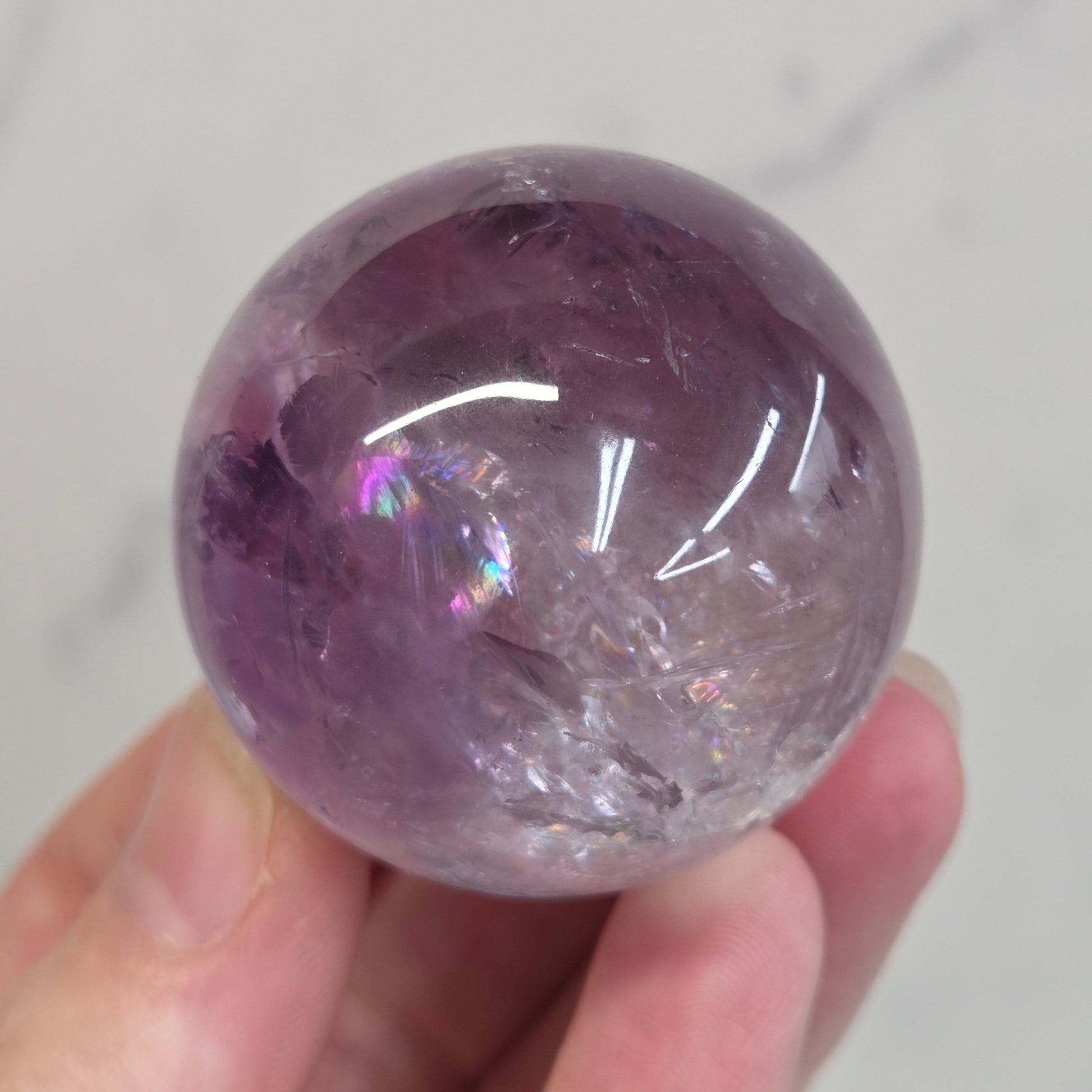 Hand holding a Phantom Amethyst sphere on a white background