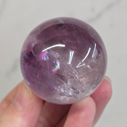 Hand holding a Phantom Amethyst sphere on a white background