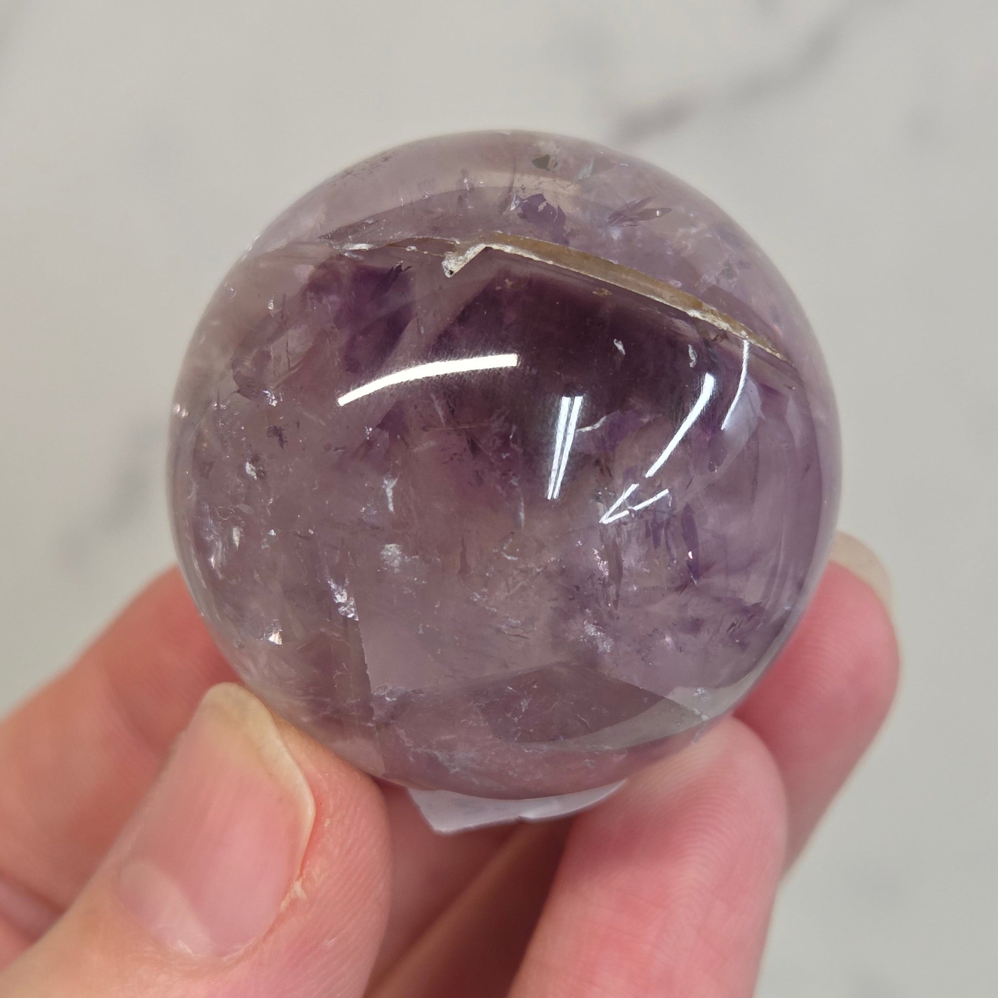 Hand holding a Phantom Amethyst sphere on a white background